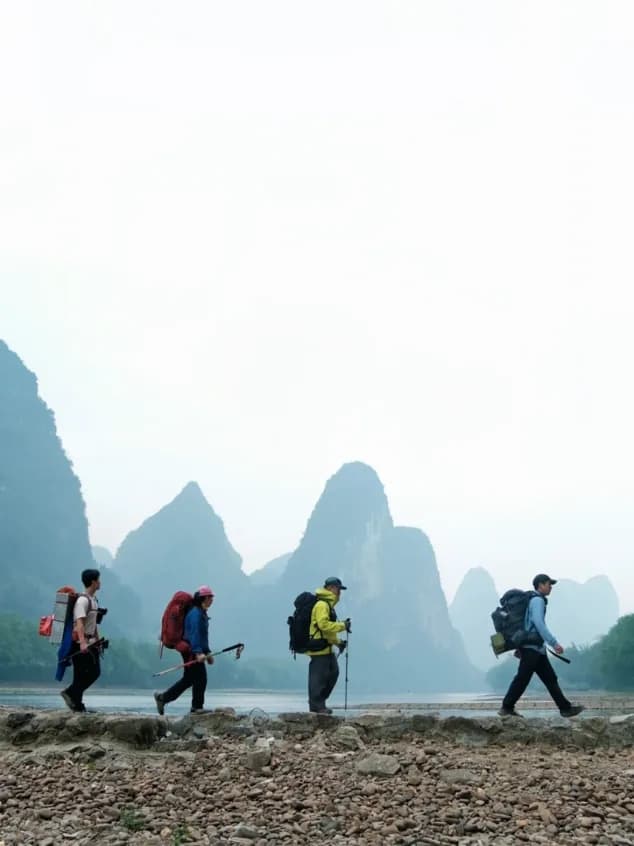 Walkers on the shingle bank of the Li River with peaks in the haze behind