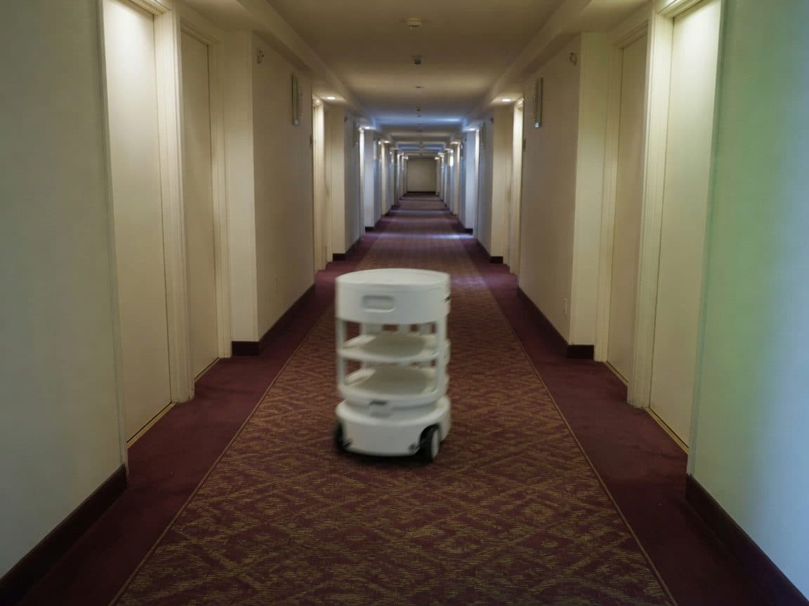 A wheeled service robot moving away down a hotel corridor, motion-blurred