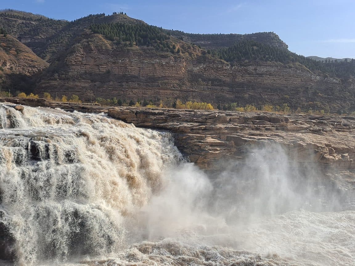 The Yellow River dropping over the Hukou falls in a wall of ochre water and spray, loess cliffs behind