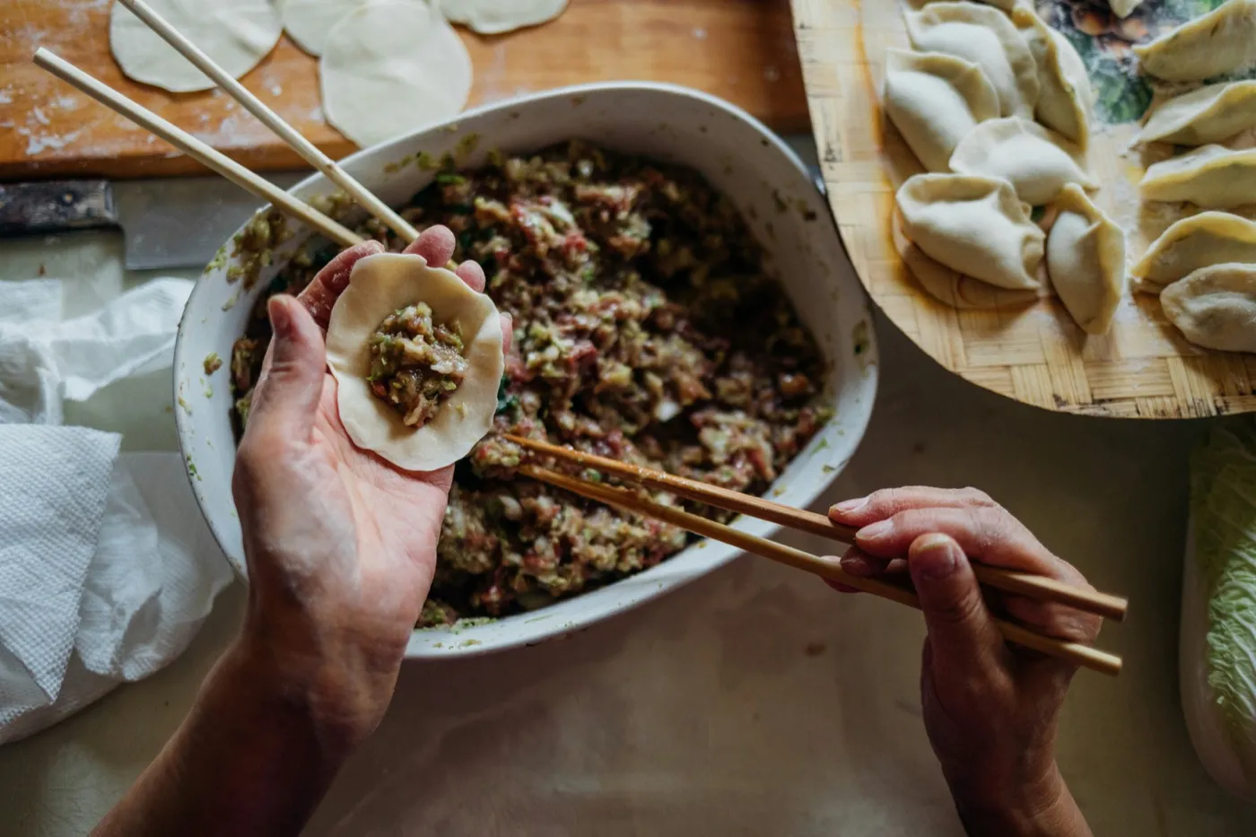 Hands filling a dumpling wrapper over a bowl of pork and cabbage filling